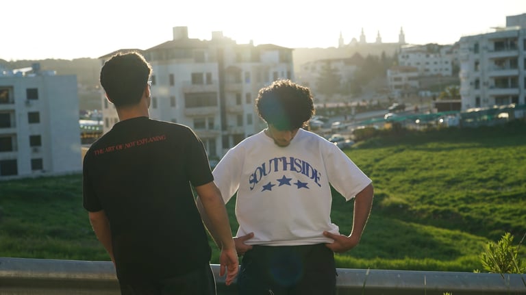 Two people from behind overlooking a residential neighborhood with apartment buildings and green fields at sunset